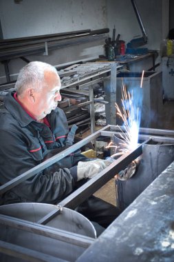 İşçi, kaynakçı, iş kıyafetleri, inşaat eldivenleri ve bir kaynak maskesiyle kaynak makinesi, Kocani Makedonya yakınlarındaki atölye çalışmasında kullanılıyor.