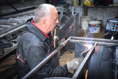 İşçi, kaynakçı, iş kıyafetleri, inşaat eldivenleri ve bir kaynak maskesiyle kaynak makinesi, Kocani Makedonya yakınlarındaki atölye çalışmasında kullanılıyor.