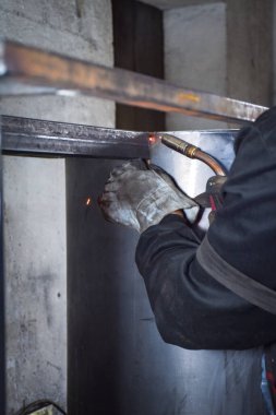 İşçi, kaynakçı, iş kıyafetleri, inşaat eldivenleri ve bir kaynak maskesiyle kaynak makinesi, Kocani Makedonya yakınlarındaki atölye çalışmasında kullanılıyor.