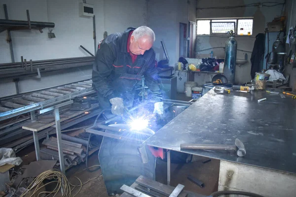 A Worker, welder in work clothes, construction gloves and a welding mask is welded with a welding machine metal product table, Workshop near Kocani Macedonia