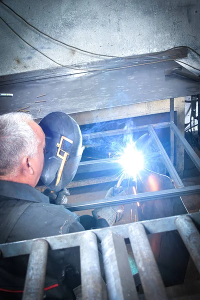 A Worker, welder in work clothes, construction gloves and a welding mask is welded with a welding machine metal product table, Workshop near Kocani Macedonia