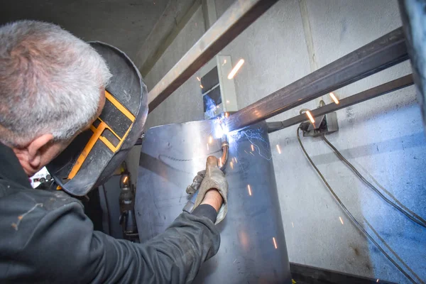 A Worker, welder in work clothes, construction gloves and a welding mask is welded with a welding machine metal product table, Workshop near Kocani Macedonia