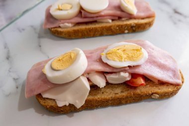 Jambonlu sandviç, haşlanmış yumurta ve beyaz mermer arka planda domates.