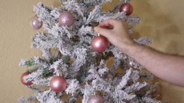 Karla kaplı bir ağaca pembe bir Noel topu yerleştiren birinin dikey videosu.