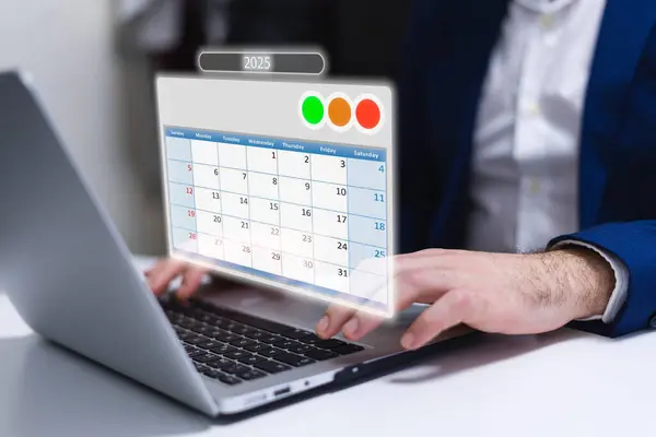 Ofisteki ekranda takvim uygulaması olan bir dizüstü bilgisayar kullanan bir iş adamı