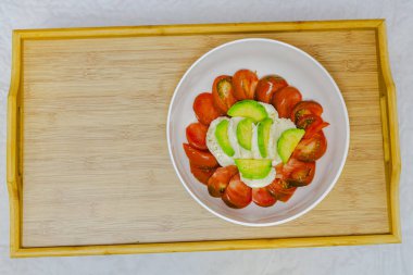 Domatesli süzme peynir ve ahşap masada beyaz tabakta salatalık.