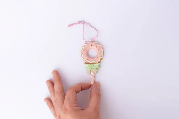 Beyaz arka planda izole edilmiş pembe ve yeşil kurdeleyle süslenmiş bir çöreği tutan bir elin yakın çekimi. Fırın, şenlik ve kutlama tasarımları için mükemmel..