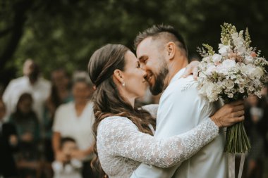 Genç gelin ve yakışıklı damat parkta öpüşüp sarılıyorlar. Birbirine aşık çift..