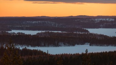 Winter forest landscape after the sun has set and colored the scenery seen from the top of a hill in Finland