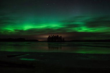 Finlandiya 'nın Pirkanmaa şehrinde kış aylarında gökyüzü aurora borealis ışığıyla yeşile boyanmış donmuş bir gölün ortasındaki ada.