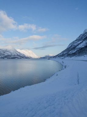 Denizin kıyısındaki karlı dağlar Kuzey Norveç 'te bir yol ve mavi bir gökyüzü ile kışın