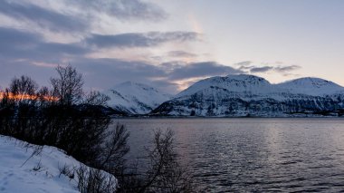 Kuzey Norveç 'te deniz kenarındaki karlı dağlar kışın gün batımında
