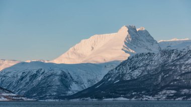 Kuzey Norveç 'te kış mevsiminde Kuzey Kutbu' nun güneş ışığıyla aydınlanan karlı dağ zirvesi.