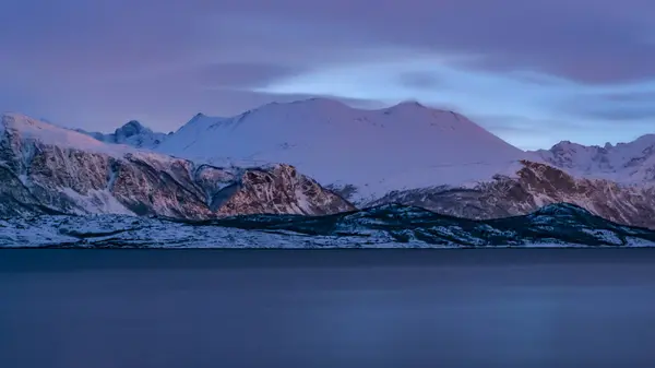 Kuzey Norveç 'te bir fiyordun yanındaki karlı dağlar kışın mavimsi alçak akşam ışığında