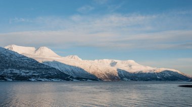 Kuzey Norveç 'te kış mevsiminde fiyortların aydınlattığı karlı dağlar.