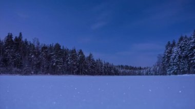 Finlandiya 'da kış gecesinin mavi ışığında, ormanın içinden geçen bulutlarla kaplı donmuş bir gölün zaman akışı