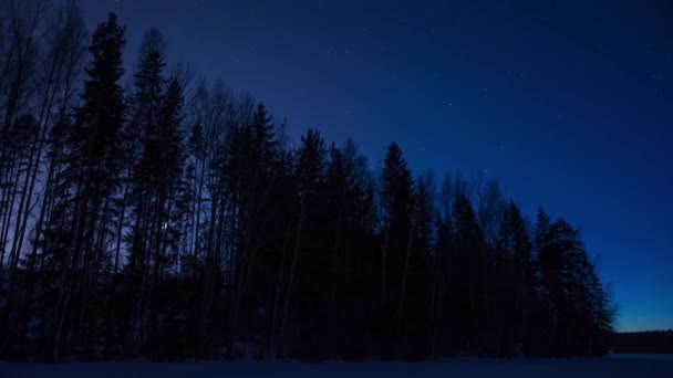Time lapse of the moon moving behind a line of trees in late evening blue light in winter in Finland