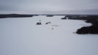 Finlandiya 'da kışın donmuş bir gölün karlı buzlu buzu üzerinde alçalan ve gökyüzünü kaplayan gri bulutlar.