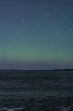 Tampere, Finlandiya 'da donmuş bir gölün üzerinde yeşil aurora borealis tonu ve dönen yıldızlar