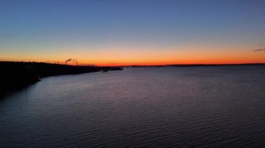 Koyu orman kıyıları ve ufuk çizgisinde günbatımının renkleriyle gölün solundan uçarak Tampere, Finlandiya 'daki binaların siluetinin arkasına geçtiler.
