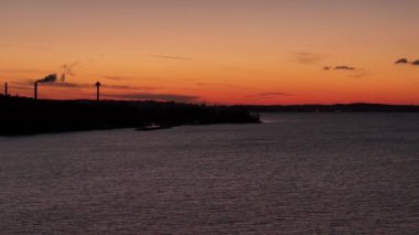 Tampere, Finlandiya 'daki binaların siluetinin arkasındaki ufukta karanlık orman kıyıları ve günbatımı renkleriyle gölün üzerinden sağa doğru yan uçuşlar.