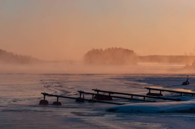 Finlandiya 'da kışın buzlu siste donmuş gölün kıyısında küçük bir liman.