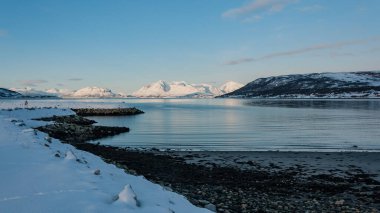 Kuzey Norveç 'te kışın fiyordun kayalık bir kıyısındaki karlı dağların manzarası