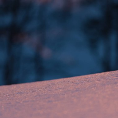 Yakın mesafeden karda gün batımı renkleri ve arka planda bulanık ağaçlar ve dallar