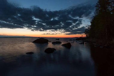 Rocks and cloud formations on the shore of lake Nasijarvi after early summer sunset in Tampere, Finland  clipart