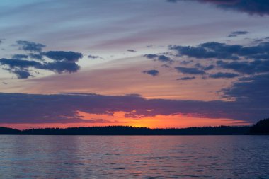 Yaz başında Nasijarvi, Tampere, Finlandiya 'da gün batımından hemen sonra bir orman ve göl üzerinde mor renkli bulutlar.