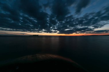 Rocks and cloud formations on the shore of calm lake Nasijarvi after early summer sunset in Tampere, Finland clipart