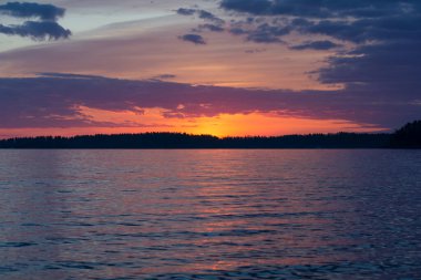 Yaz başında Nasijarvi, Tampere, Finlandiya 'da gün batımından hemen sonra bir orman ve göl üzerinde mor renkli bulutlar.