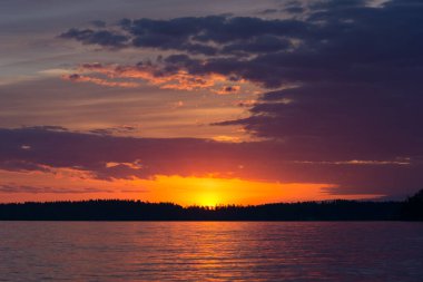 Yazın başında Nasijarvi, Tampere, Finlandiya 'da bir orman ve göl üzerinde gün batımından hemen sonra renkli gökyüzü ve bulutlar