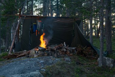 Yazın Inari, Lapland, Finlandiya 'da önünde ateş olan bir kayanın üzerinde laavu barınağı olan bir kamp.