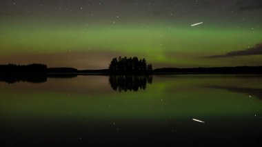 Finlandiya 'nın güneyinde sakin bir göl yüzeyine yansıyan ada ve aurora borealis renkleri
