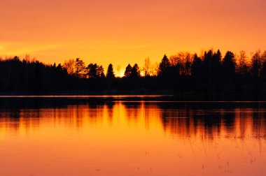 Günbatımının renkleri Batı Finlandiya 'da ilkbaharda sakin bir gölden yansımaktadır.