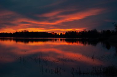 Günbatımının renkleri Batı Finlandiya 'da ilkbaharda sakin bir gölden yansımaktadır.
