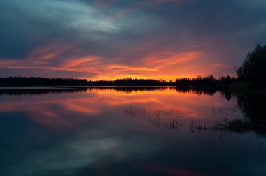 Günbatımının renkleri Batı Finlandiya 'da ilkbaharda sakin bir gölden yansımaktadır.