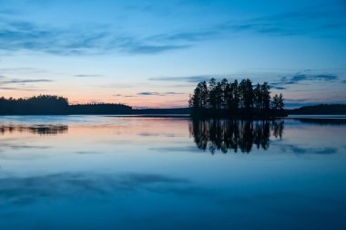 Finlandiya ormanlarında tahtadan bir adayla sakin bir gölün akşam manzarası