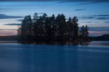 Finlandiya ormanlarında tahtadan bir adayla sakin bir gölün akşam manzarası