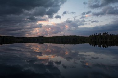 Finlandiya 'da sakin bir gölün yüzeyine yansıyan bulutlar ve ormanlar
