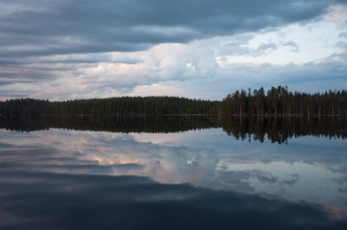 Finlandiya 'da sakin bir gölün yüzeyine yansıyan bulutlar ve ormanlar