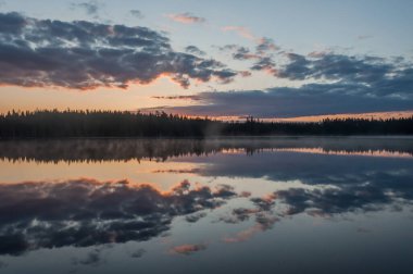 Finlandiya 'da sakin bir gölün yüzeyine yansıyan bulutlar ve ormanlar