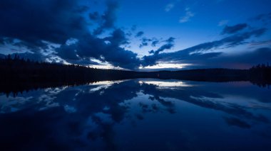 Finlandiya 'da ormanlar yüzeye yansıyan sakin bir göl kenarındaki mavi ışıklı akşam manzarası