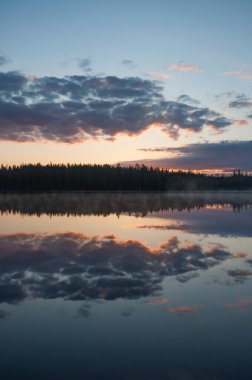 Finlandiya 'da sakin bir gölün yüzeyine yansıyan bulutlar ve ormanlar