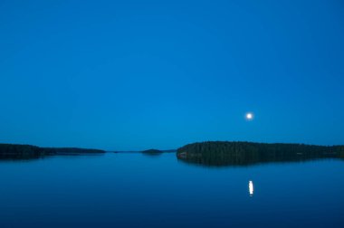 Yaz başında Finlandiya 'da sakin bir gölün kenarında ay yüzeye yansıyor.