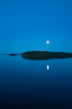 Yaz başında Finlandiya 'da sakin bir gölün kenarında ay yüzeye yansıyor.