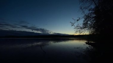 Finlandiya ormanlarındaki bir gölün kenarında yükselen güneşin gökyüzünü renklendirdiği bir yaz gecesinin hızlandırılması