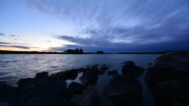 Finlandiya ormanlarındaki bir gölün kıyısında gökyüzünün kara bulutlarla kaplı olduğu bir yaz akşamının hızlandırılması