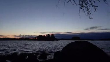 Finlandiya ormanlarındaki bir gölün kıyısında gökyüzünün kara bulutlarla kaplı olduğu bir yaz akşamının hızlandırılması